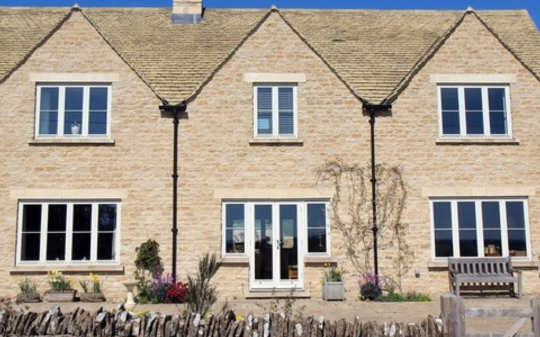 Traditional Cotswold-style stone house with white windows.