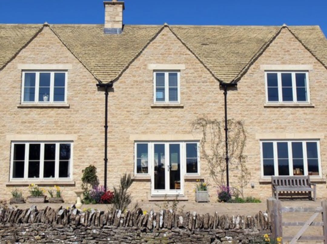 Traditional Cotswold-style stone house with white windows.